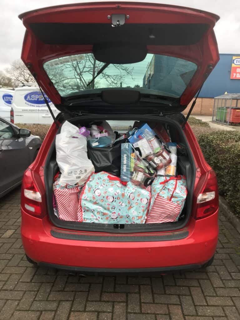 Open boot of a red car shows interior full of presents