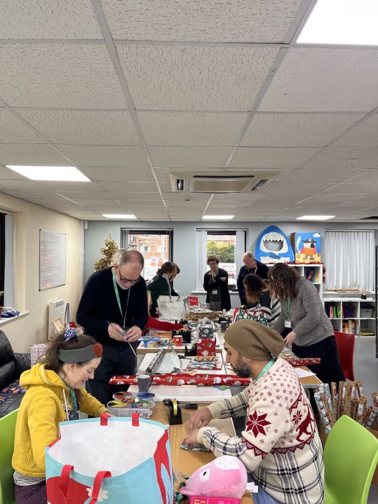a group of people chat and wrap Christmas presents on a large table