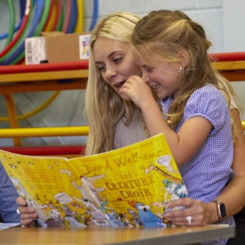 Two children reading a colourful storybook together in a community centre, promoting literacy and family bonding.
